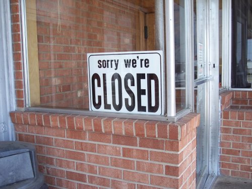 A sign in a window reads "Sorry, we're CLOSED" against a brick wall background.