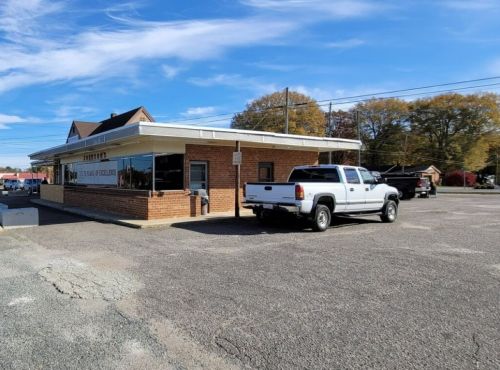 A white pickup truck parked outside a brick building with a sign, under a clear blue sky.