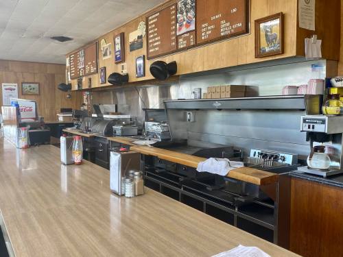 A diner counter with a grill, condiments, and menu boards on the wall, featuring a classic retro design.
