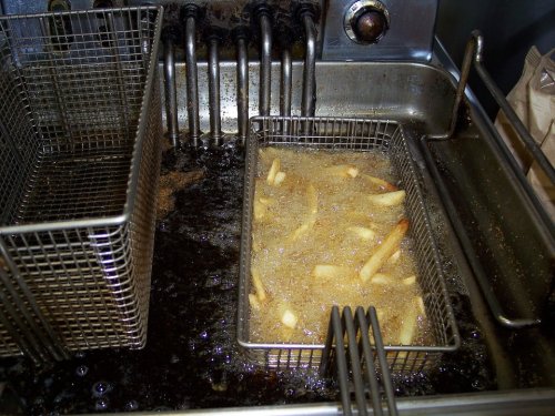 A deep fryer with a basket of frying French fries in hot oil, next to an empty basket.