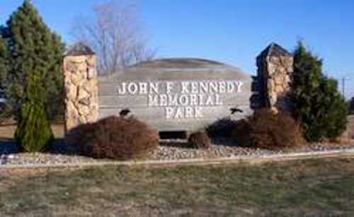 Sign for John F. Kennedy Memorial Park, featuring stone pillars and landscaping in a grassy area.