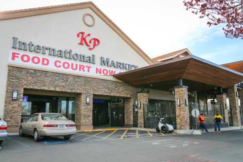 Exterior of KP International Market with a food court sign, featuring a stone facade and two workers outside.