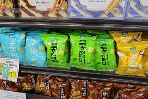 A shelf displaying colorful Korean rice snack packages in green and yellow, with a sign for Korean rice snacks.