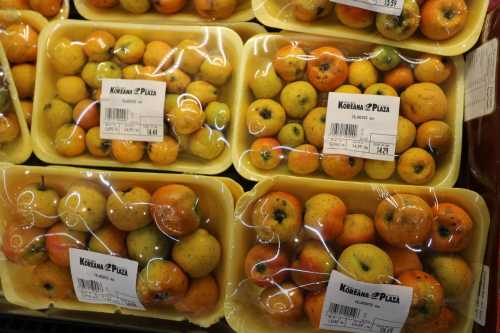 Baskets of small oranges and yellow fruits, wrapped in plastic, displayed in a grocery store.