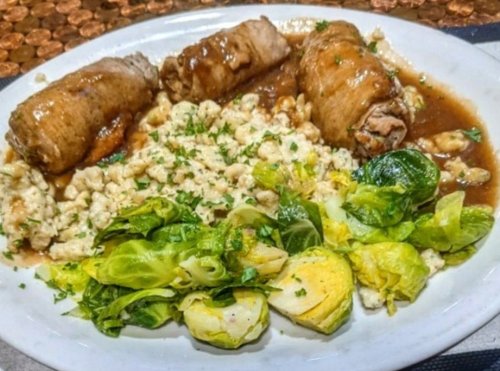 A plate featuring rolled meat in gravy, creamy rice, and a side of sautéed Brussels sprouts.