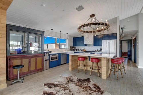 Modern kitchen with blue cabinets, a large island, red bar stools, and rustic decor, featuring a cowhide rug.
