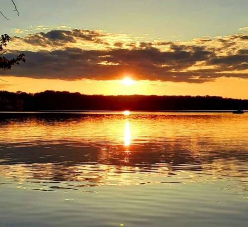 A serene sunset over a calm lake, with vibrant orange and yellow hues reflecting on the water's surface.