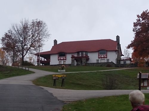 A large, two-story house with a red roof, surrounded by trees and a winding path leading to it.