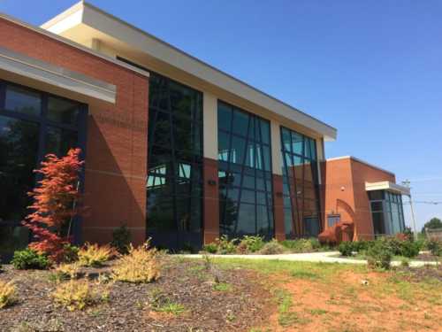 Modern building with large glass windows, brick exterior, and landscaped garden under a clear blue sky.