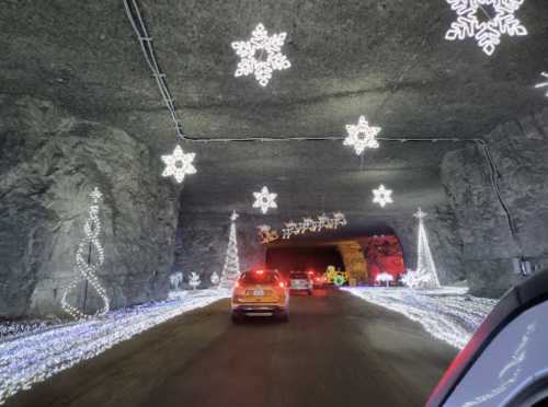 Cars driving through a tunnel decorated with festive snowflake and Christmas tree lights.