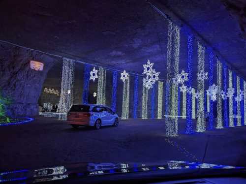 A car drives through a tunnel adorned with colorful holiday lights and snowflake decorations.