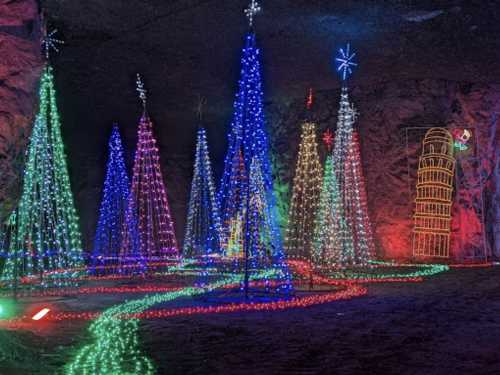 Colorful illuminated Christmas trees in a cave, surrounded by festive lights and decorations.