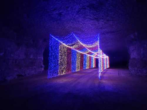 A colorful display of lights draped in a cave, creating a vibrant tunnel effect against a dark background.