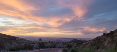 A scenic view of a winding road leading to a city, with vibrant sunset colors illuminating the sky.