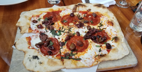 A freshly baked pizza topped with pepperoni, olives, and herbs on a wooden board.