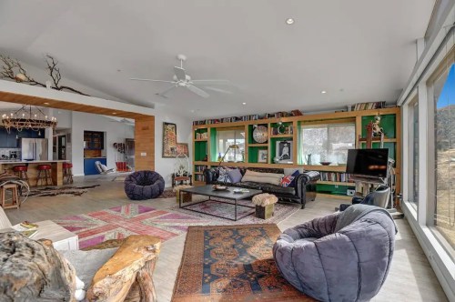 A modern living room with colorful decor, large windows, and cozy seating, featuring bookshelves and a stylish rug.