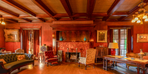 A vintage living room with wooden beams, rich red walls, elegant furniture, and a cozy fireplace.