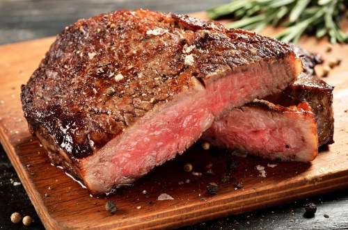 A perfectly cooked steak with a seared crust, resting on a wooden cutting board, showcasing a juicy pink interior.