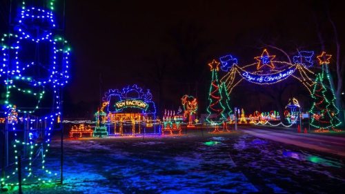 Colorful holiday lights illuminate a festive scene with trees, stars, and decorations against a dark night sky.