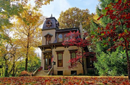 A charming house surrounded by vibrant autumn foliage and colorful trees under a clear blue sky.