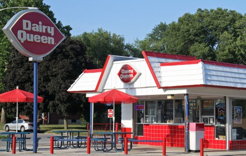 A Dairy Queen restaurant with a red and white exterior, outdoor seating, and a sign indicating it's open.