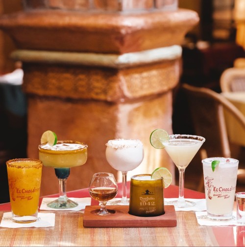 A variety of colorful cocktails and drinks arranged on a table, featuring garnishes and decorative glasses.