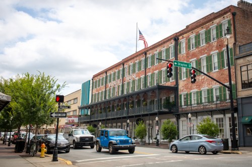 Historic building with green shutters, American flag, and traffic at a street intersection on a cloudy day.