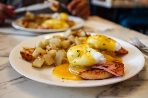 A plate of eggs Benedict with ham and poached eggs, served with golden-brown diced potatoes on the side.