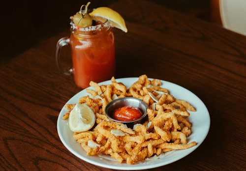 A plate of crispy fried calamari with a lemon wedge and dipping sauce, alongside a refreshing drink with a lemon slice.