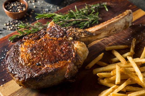 A juicy ribeye steak with herbs, served alongside crispy French fries on a wooden cutting board.