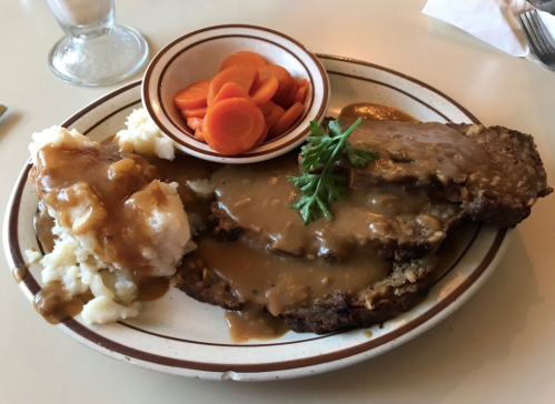 A plate of meatloaf with gravy, mashed potatoes, and a side of carrots.