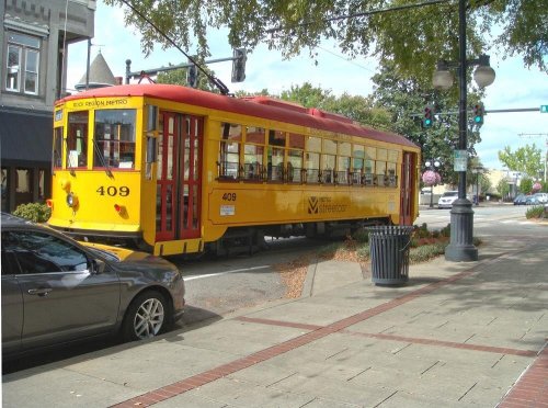 A bright yellow streetcar with red accents parked on a city street, surrounded by trees and buildings.