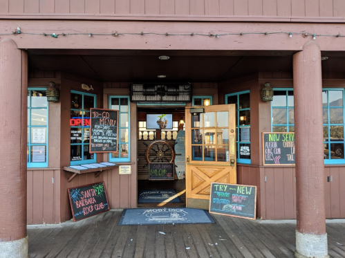 Entrance of a rustic restaurant with wooden doors, blue trim, and various signs displaying menus and specials.