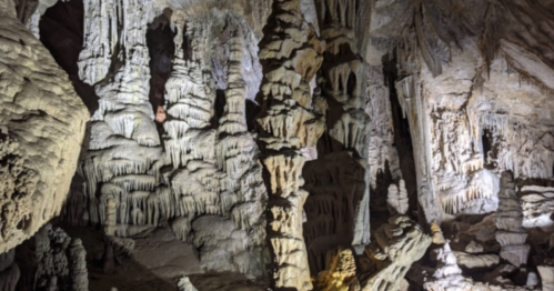 Stalactites and stalagmites in a dimly lit cave, showcasing intricate rock formations and textures.