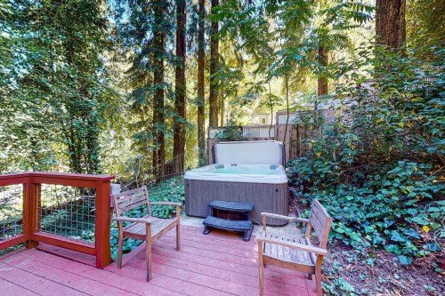 A hot tub surrounded by tall trees, with wooden chairs on a deck in a serene outdoor setting.