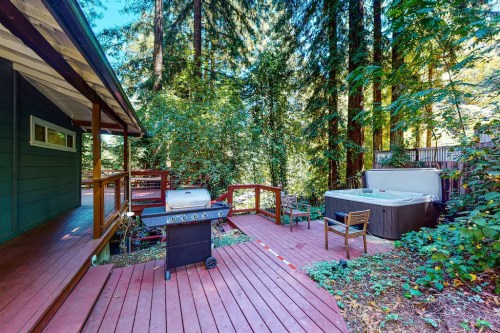 A wooden deck with a grill and hot tub, surrounded by tall trees in a serene outdoor setting.
