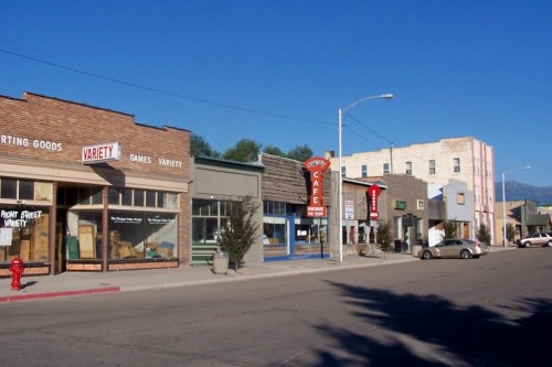 A quiet street scene featuring small shops, a café, and clear blue skies in a small town.
