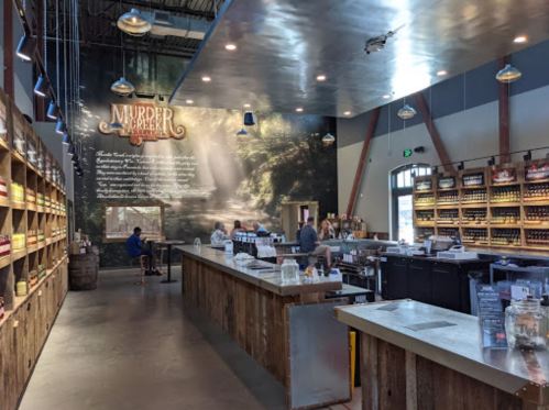 Interior of a rustic tasting room with wooden shelves, a bar, and a mural featuring trees and text on the wall.