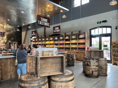A rustic tasting room with wooden shelves filled with bottles, a bar area, and barrels, creating a warm, inviting atmosphere.
