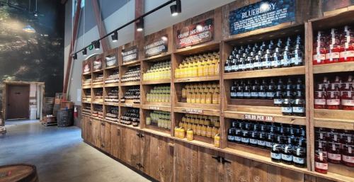 A wooden shelf displays various bottles of beverages, including fruit juices and syrups, in a rustic setting.