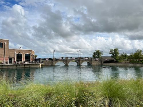 A scenic view of a bridge over a calm waterway, with cloudy skies and greenery in the foreground.