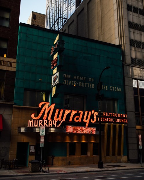 Exterior of Murray's Restaurant, featuring a vintage neon sign and a teal building facade in an urban setting.