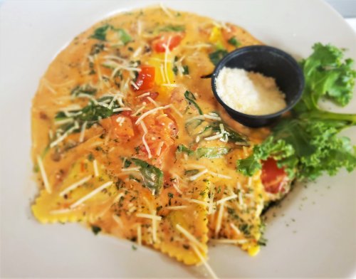 A plate of ravioli in a creamy sauce, topped with tomatoes, spinach, and cheese, served with a side of grated cheese.