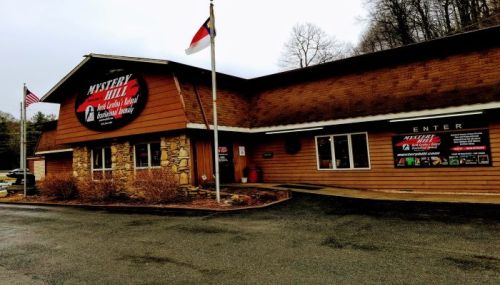 Exterior of Mystery Hill, a wooden building with a stone facade, featuring signs and flags in a rural setting.