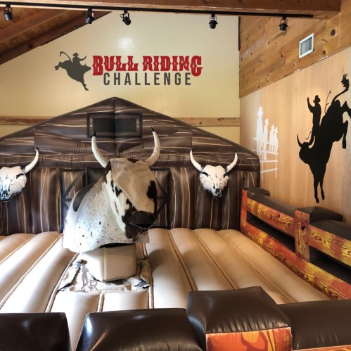 A bull riding challenge setup featuring a mechanical bull and cowboy-themed decor in a rustic interior.