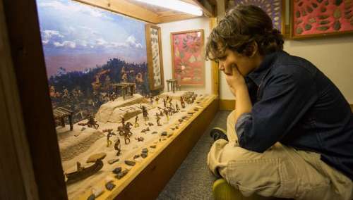 A child observes a detailed miniature scene with figures and structures in a display case.