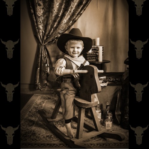 A young child in a cowboy hat smiles while sitting on a rocking horse, surrounded by a cozy, vintage setting.