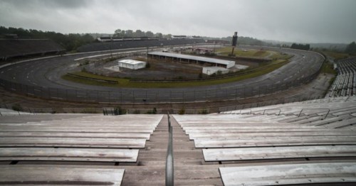 A view of an empty racetrack and grandstands under a cloudy sky, with a desolate atmosphere.