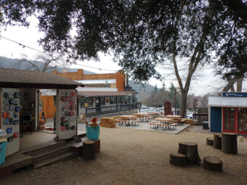 A scenic outdoor area with climbing holds, picnic tables, and buildings surrounded by trees on a cloudy day.