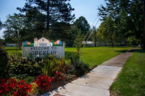 Welcome sign for Oberlin, surrounded by greenery and colorful flowers, with a sidewalk leading into the area.
